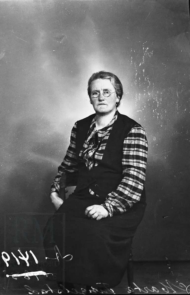 Portrett av Marta Tingelstad, sittende iført skjørt med vest til og en rutet bluse.
