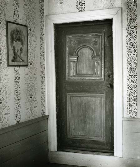En innerdörr med snidade dörrspeglar. Runt dörren är väggarna målade med schablonmåleri.