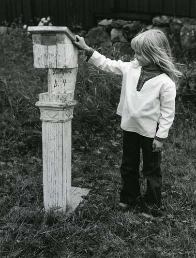 En flicka står intill en vägskiftespåle vid Lökagården, Alfta på 1980-tal.
