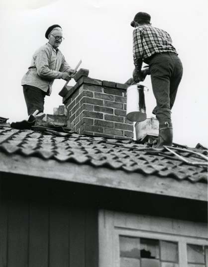 Två personer står på ett tak och renoverar en skorsten.
