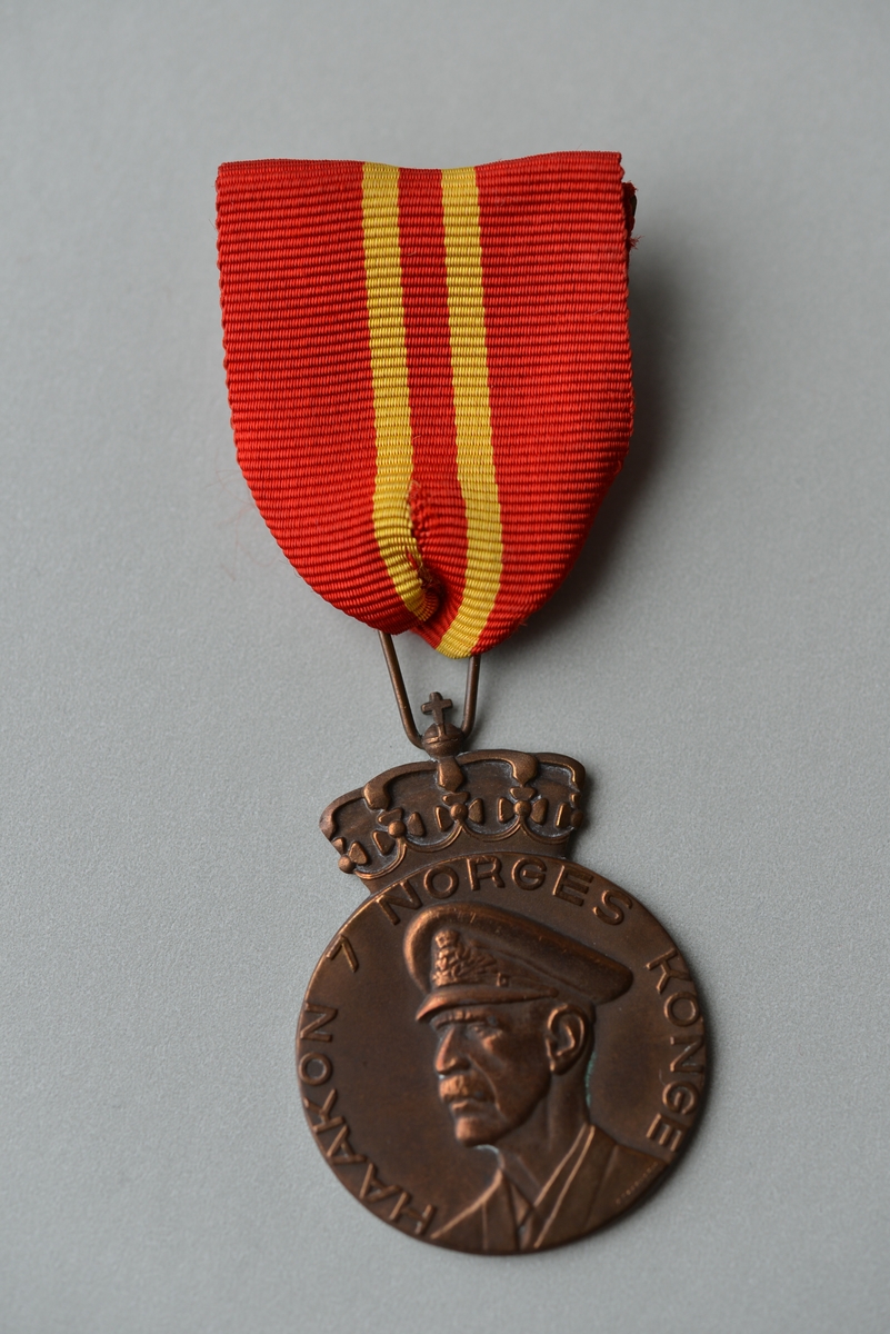 Kong Haakon VII i profil med uniformslue på framsida.
Teksten på baksida er omkransa av ei dekorbord.
Ei krune er ein del av toppen på sjølve medaljen.
