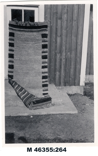 Svartvitt foto av flossamatta, utomhus.

Inskrivet i huvudbok 1983.
Montering/Ram: Ej ramad