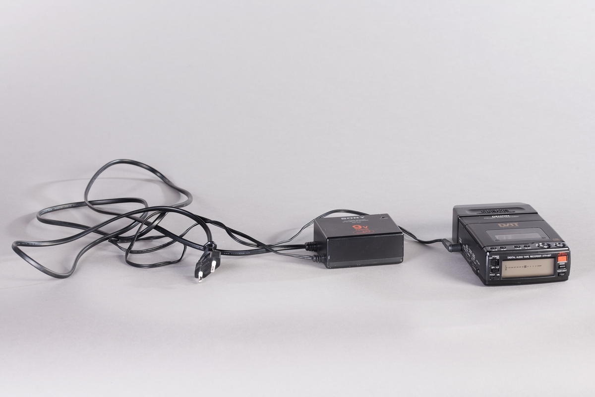 Bærbar og kompakt DAT-spiller i svart innretning med separat batteriholder og strømforsyning. Spilleren har innebygd mikrofonforsterker (analog inngang). I esken 1/2 finnes også bruksanvisning, 6 kassettbånd og en perm med foto og sanglister. Strømadapter finnes i eske 2/2.