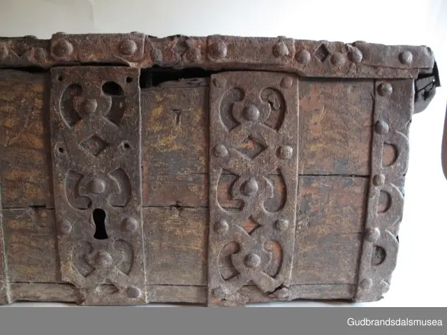 "Rik gjenombroten jarning over heile skrinet. Gamal type, alder uviss. Fra Vestre Gausdal". (Jf. "Katalog for Lom Bygdesamling,1925"). 
Skrinet har 3 rom, nøkkelhullslås og jernhandtak på sidene. Lokket er satt sammen av 2 bord, er festet til utsiden på bakstykket med to hengselbeslag og har 2 sidelister festet med trenagler. Bunnen er satt sammen av 2 bord, festet til hverandre med 2 forsenka trenagler; bunnen er festet til skrinrammen med trenagler.  Skrinrammen er tappet og forsterket med hjørnekantbeslag utvendig. 
Skrinet har jernbeslag med gjennombrutt mønster, 5 stk. B: 6,5 x L: 45 cm på lokk, 3 på hhv. bakstykke, front og sidestykker B: 6,5 x 20 cm. Lokket har ett låsbeslag og de to øvre hengselbeslag festet på innsiden, de to nedre hengselbeslag er festet på utsiden av bakstykket. Alle beslag er festet med store jernnagler samt festet under bunn på skrinet. De to hengselbeslag har også gjennombrutt mønster.  Nøkkelhullslåsen mangler låsanordning på innsiden.
DEKOR. Malingen har blitt beskyttet med et lag ferniss el.l., noe som ble vanlig fra begynnelsen av 1700-tallet. Ingen skurddekor. I stedet er beslag av jern brukt som dekorelement, noe som periodemessig kan peke på 1600-tallet, tidlig 1700-tallet, der treskurden ikke var fremherskende. Liknende dekorbruk finner du på LBY0328. Skrinet har gjennombrutt mønster på beslag og store jernnagler som beslagfeste. Treverket som synes mellom beslagene er malt med horisontale bølgestrukturer i gul og brun. Den dominerende dekorfargen er brun og gul, men det finnes små rester av blå eller blågrønn på lokk, sidelister på lokk, front og bunnkant på bakstykket samt av gul på frontbeslag. Innsiden av lokket er malt i terracottarød nyanse. Tradisjonelt fremkom denne fargen ved bruk av saft fra orr blandet med spytt, som ble smurt ut over treet. 
BRUK. Før kofferten kom i bruk hadde man reiseskrinet, som ble brukt til oppbevaring av bl.a. klær, verdisaker og mat på reiser. Skrinet hadde ofte et eller to mindre, smale rom langs den ene skrinsiden og ett større rom. De fleste reiseskrin var i tillegg forsterket med jernbeslag langs alle kanter og med en solid nøkkelhullås til sikring mot støt, slag og tyveri.