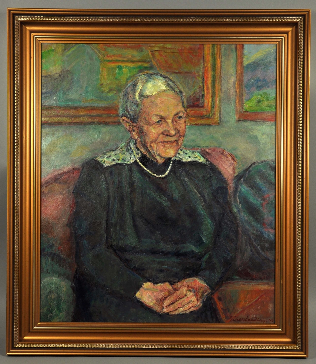 Portrett av en eldre dame, halvfigur sittende i en sofa i trekvartprofil vendt mot høyre. Kvinnen har grått hår, er iført en mørk kjole med lysere felt på skuldrene og har perlekjede rundt halsen. På veggen bak sofaen henger to malerier. Rammet inn i ny ramme.