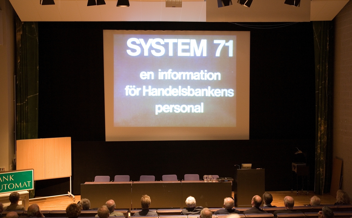 Seminarium "Hur IT förändrade bankvärlden" i Hörsalen på Tekniska museet. Här visas en film om System 71, som var Handelsbankens datasystem. En tidig bankautomat från Tekniska museets samling står på vänster sida i lokalen. (TM39474)