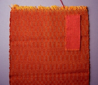 Två vävprover, gåsögonmönstrade möbeltyger i bomull och ull. Två olika färgställningar; ett orangerött och ett rosarött.
WLHF-0775:1 Varp i orange bomullsgarn nr 16/2.Inslag i rött 1-trådigt ullgarn; möbeltygsgarn. Två trådar tillsammans per inslag.Mått: 290 mm, 350 mm.
WLHF-0775:2 Varp i orange bomullsgarn nr 16/2.Inslag i ljusrött 1-trådigt ullgarn; möbeltygsgarn. Två trådar tillsammans per inslag. Mått: 53 mm, 127 mm.WLHF-0775:2 liknar WLHF-0559 som vävdes för Gästis 1991 till stolarna i restaurangen. Foto på stolar (2007 ngt blekta) samt scannat tidningsurklipp finns i datamapp "Tillbehör". Solvnota finns.