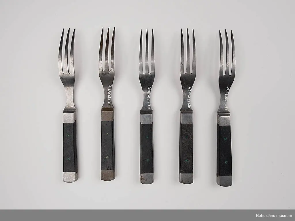 Trekloig gaffel med svart träskaft. I skaftets båda ändar metallskoning, 5 st.
Snarlik UM017095 och UM017096. Snarlik kniv UM017098:1-4.