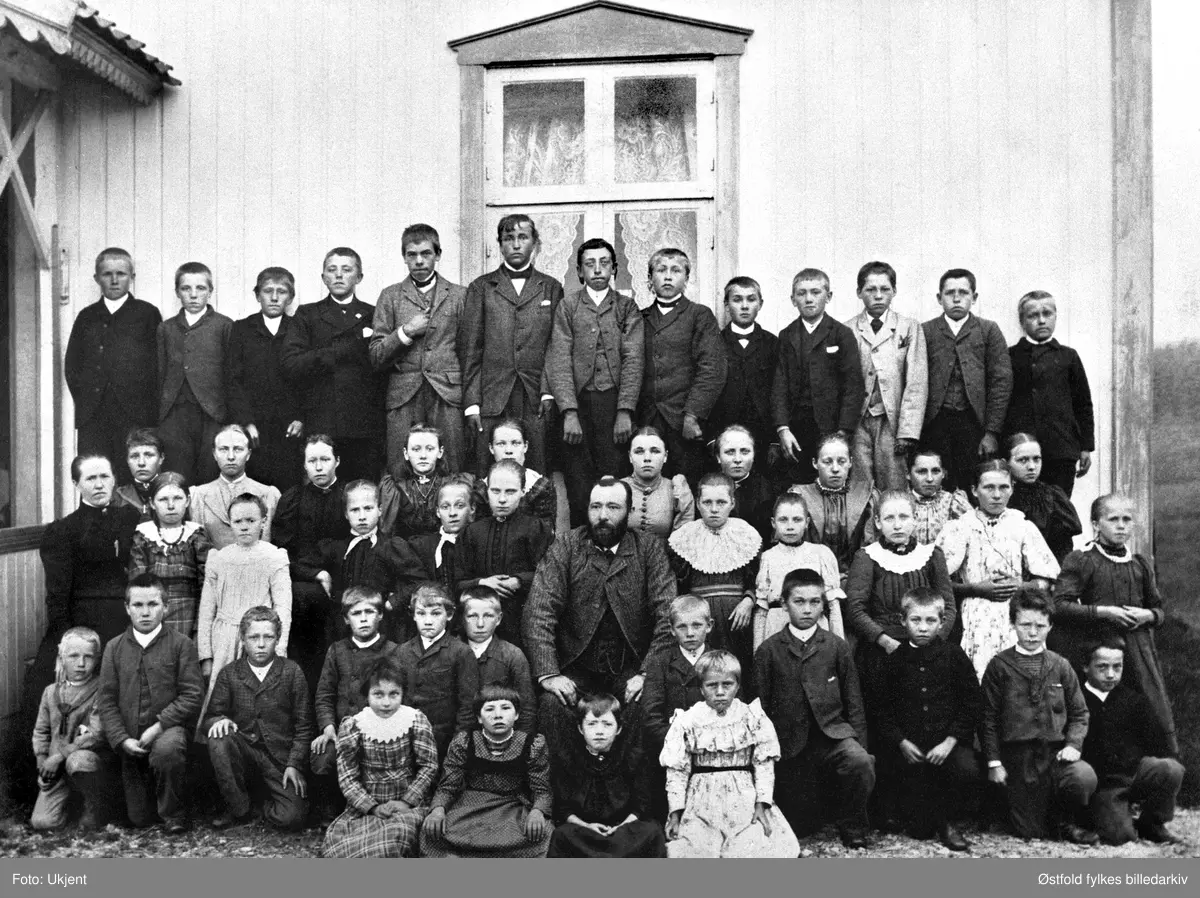 Jelsnes skole med lærer Strand og madam Tilla Strand 1895-96. Navneliste med plassering på bakside av fotokort %