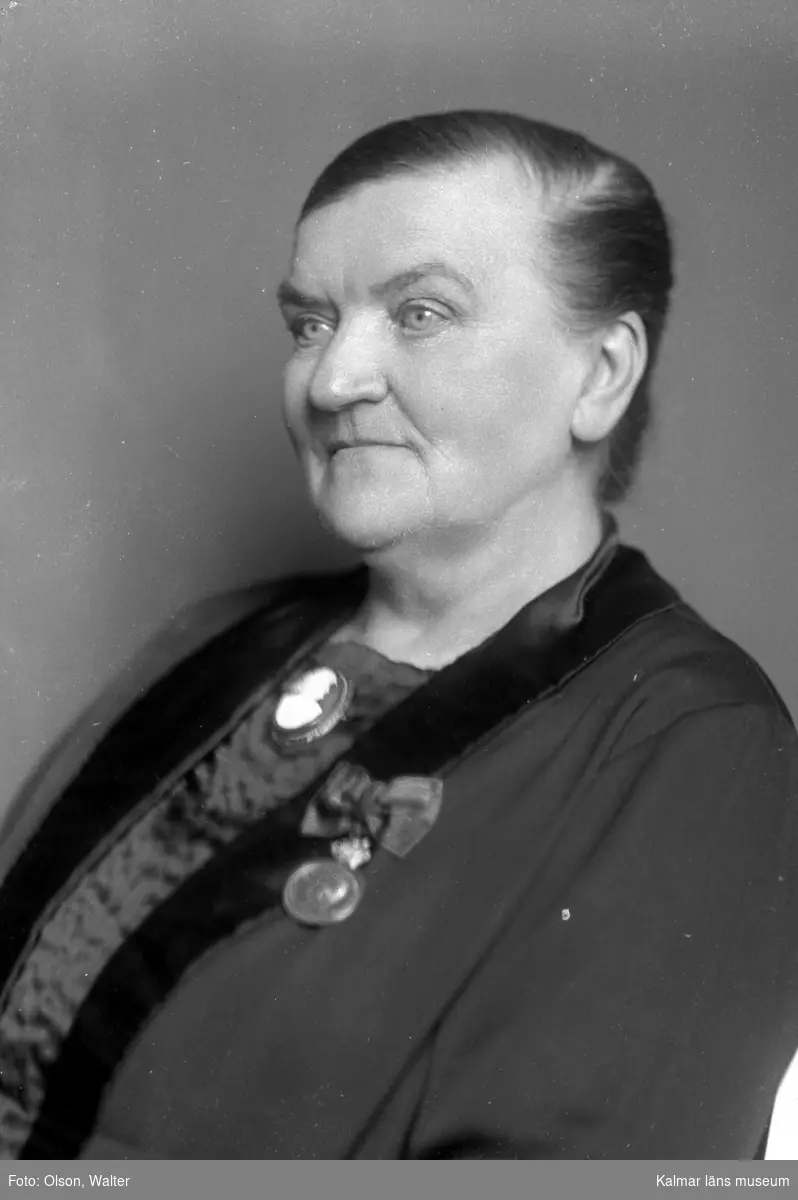 Ateljébild på Kristvalla sockens barnmorska Britta Österström. Hon tjänstgjorde i Kristvalla 1880-1930 och fick vid sin avgång medalj för lång och trogen tjänst. Britta Österström levde 1855-1937.