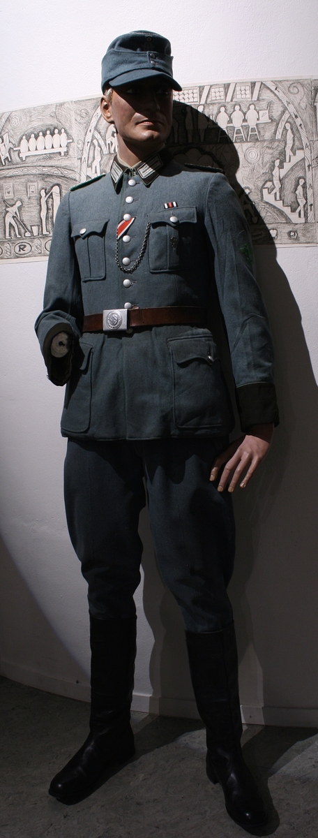 Full uniform med støvler. På brystet har den en pins (Politiets dag 1942), en bånd (Minne-/deltakermedalje 1914-1918) og EK. 2. klasse bånd. Den har også fløyte i brystlommen. 

Skulderdistinksjoner til en oberwachtmeister

I lommen var det stoff lapper og sytråd med nål. 

På beltet har den pistolhylster med Walther PP magasin.