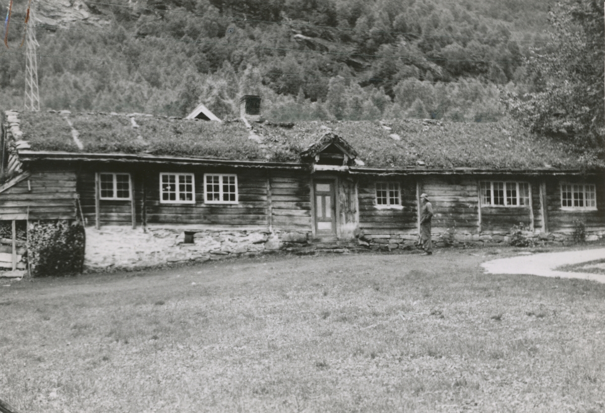 Et stovehus i Øvstegara på Løset i Stordal. Ein mann i regnfrakk står foran huset.