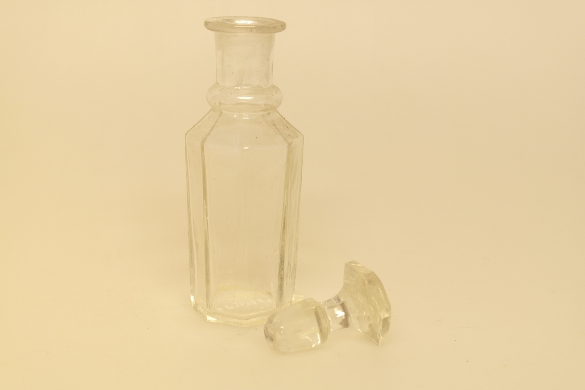 Kryddersett bestående av stativ (a), to flasker (b, c, f) og to glass (d-e).
A) Krydderstativ av tre og støpt messing. Messingkant rundt 4 sirkelåpninger. Fire balusterformede messingbein.
B) Flaske i støpt glass med glasspropp (F)
C) Flaske i støpt glass
D) Støpt glass