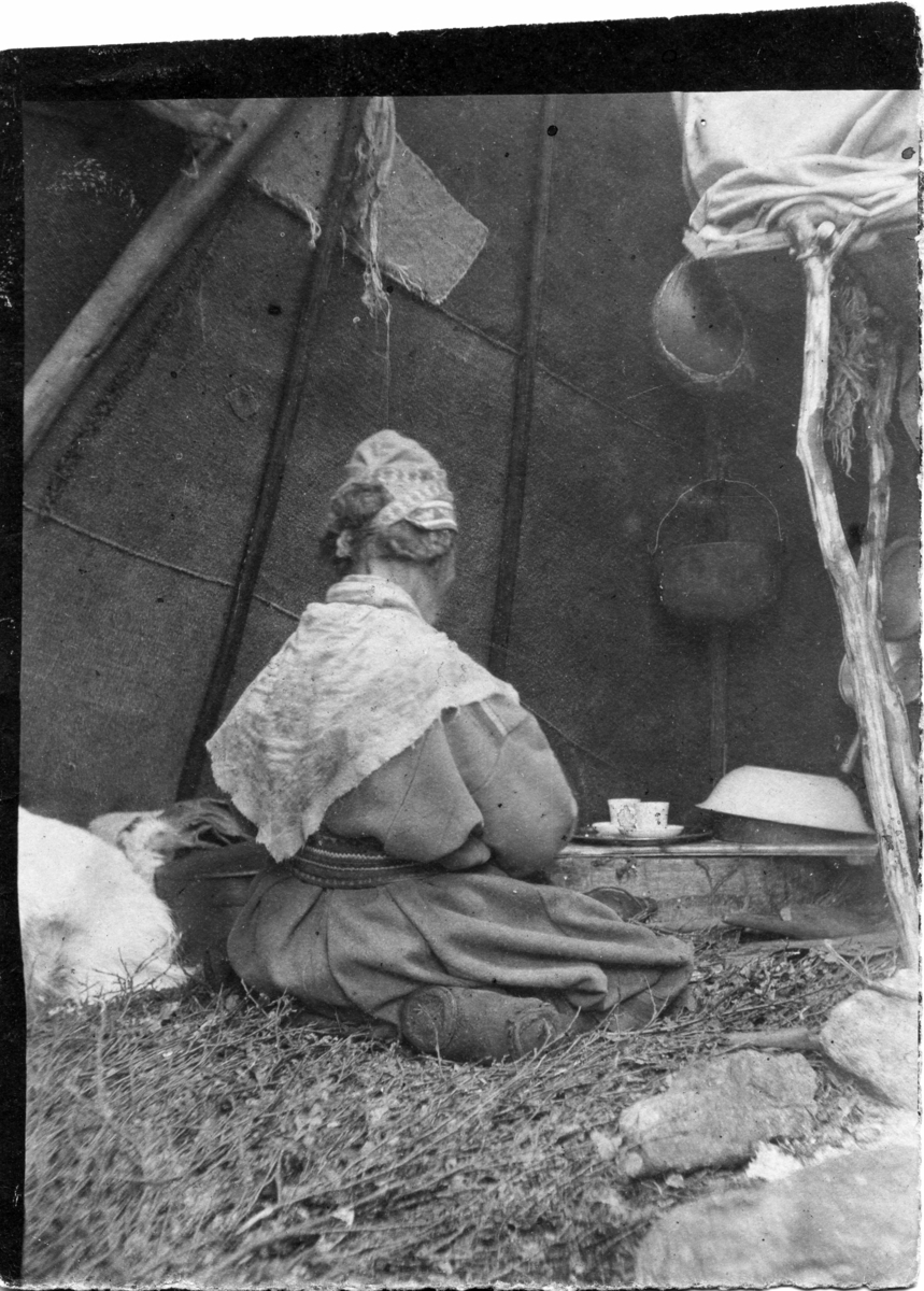 John Bauers Lapplandsresa sommaren 1904. I ett sameläger sitter en kvinna inne i kåtan med husgeråd omkring sig.