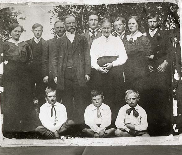 Grupporträtt av män, kvinnor och barn i utomhusmiljö. Alla är uppklädda i stiliga kläder. I mitten längst bak med mörk slips står författaren Albert viksten.