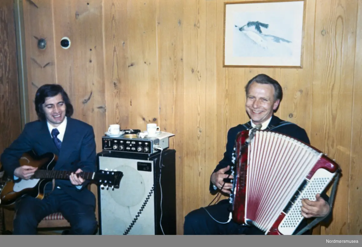 Øivind Stadsnes, gitar og Gunnar Tømmervåg, trekkspill, spiller til i et bryllup, Fosna Hotell, på 1970-tallet. På 1950-tallet arbeidet disse to sammen i musikkforretningen til Arnold Drage på Vågekaia. Originalfotoet er i Gunnar Tømmervågs eie. Fra Nordmøre museums fotosamlinger.