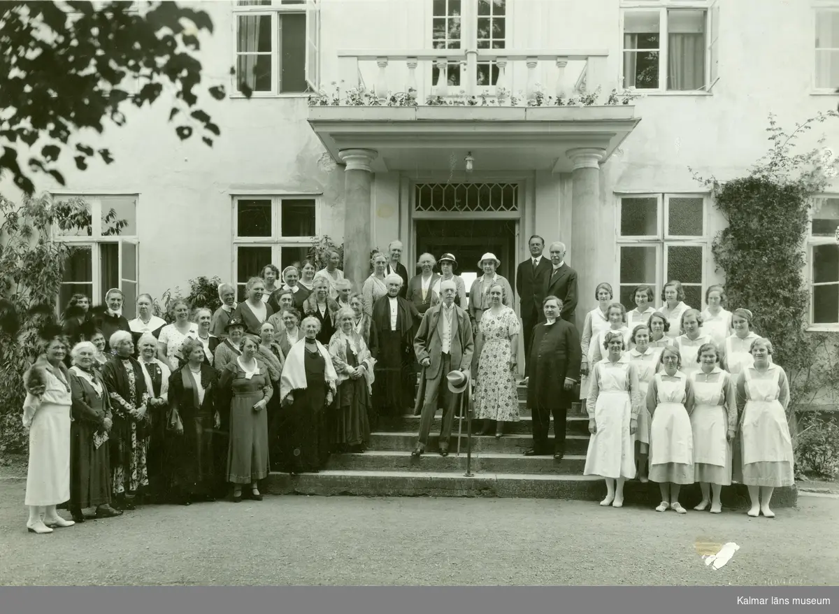 Kung Gustav V på trappan till drottning Viktorias vilohem år 1938, omgiven av personal och gäster.