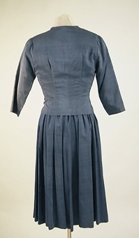 Jacka av blått shantungsiden tillhörande klänning 106163:1.
Knäppes med tryckknappar, tre st klädda knappar som dekoration.
Fodrad med ett blått viskosfoder.
Sydd av givaren på 1950-talet.
