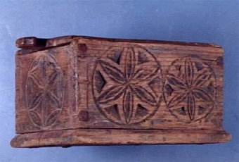 Kryddlåda med skjutlock, sprucken kring flera spikhål, har rester av färg, inskription och karvsnitt i lockets insida