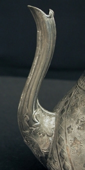 Kaffekanna av Britannia med snett gående ornamentala fält på buken, handtag och fyra fötter. Knappen på locket är i form av en fågel.
