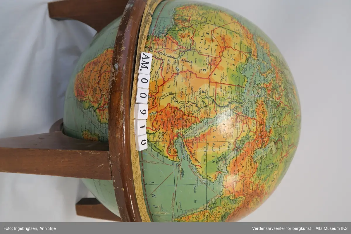 Globus med kart i farger og stedsnavn på engelsk. Beholderen er i tre, med fire buede foter under og en sirkelrund kant oppå disse fotene.