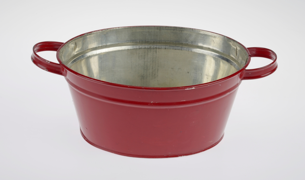 En oval balje laget av blikk som er rødlakkert men sølvfarget på innsiden. I hver side er det hanker som trolig er loddet på. Baljen er laget som leketøy og kan ha blitt brukt som oppvaskbalje eller badebalje (eller begge deler).
