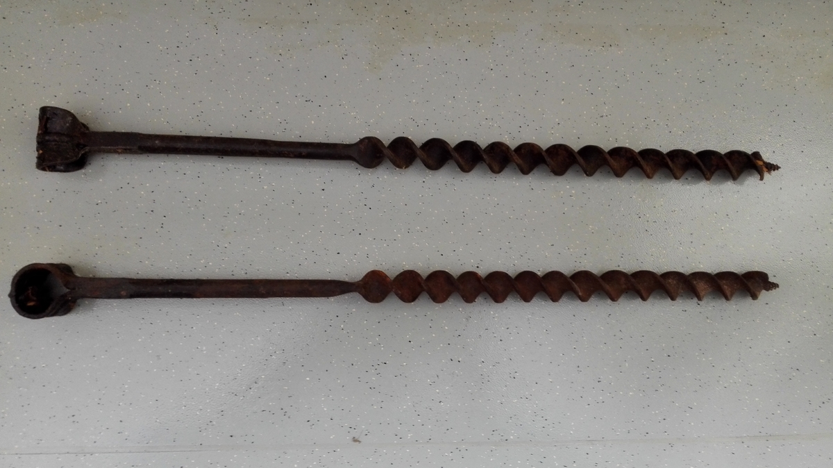 To identiske store spiralborar med bøyle (hol) for isetjing av handtak på toppen av boren. Handtak manglar.