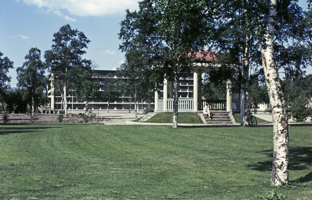 Paviljongen i parken, dame som sitter på trappa, i bakgrunnen Gymnaset.