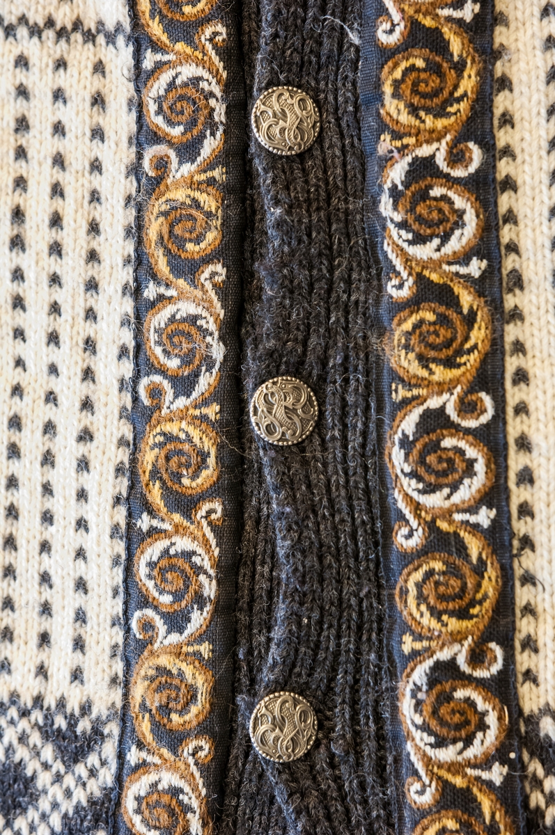 Strikket jakke med lange ermer i to farger. Pyntebånd langs hals og stolpe, brun og kvit. 7 metallknapper. Mønster: Ol-genseren fra Lake Placid 1980. Design: Dale of Norway