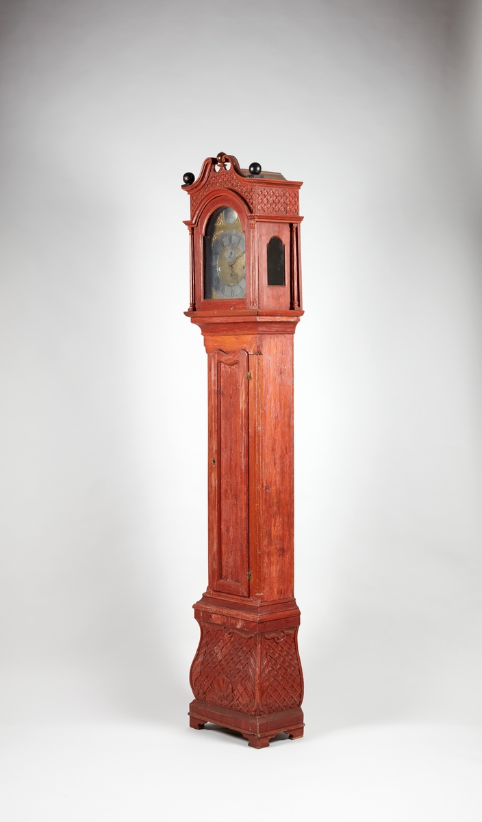 Rødmalt gulvur med forsiringer i form av nettverk, sped, stilisert akantus og rocaille. Urverket har sekund-, minutt- og datoviser og er forsynt med spillverk med to melodier.