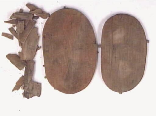 En svepask, i delar. Delarna består av ett lock, en botten samt ett fragmentariskt svep. På locket och bottnen syns sju kvarsittande träpligg.