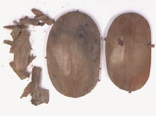 En svepask, i delar. Delarna består av ett lock, en botten samt ett fragmentariskt svep. På locket och bottnen syns sju kvarsittande träpligg.
