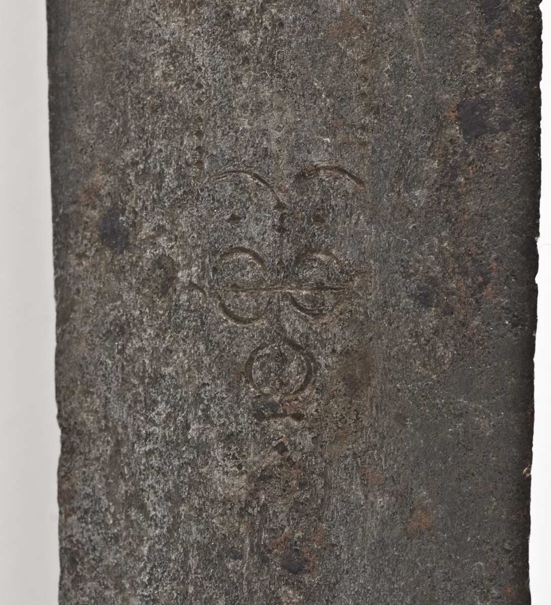 Rund pæreformet knapp med 10 fasetter  Tregrep. Flate svakt opp og nedbøyde  parerstenger med som ender i to fliker. Punslet dekor på parerstengene.
Asymetrisk kurvfeste med nyreformet parerplate på innsiden Prereplaten på utsiden er borte. Sidebøyler og håmdbøyle er formet av flate bånd. Skade på bånd på utsiden.
Tveegget rett klinge med  ovaklt  tverrsnitt  og to korte blodrender. Klingen har innskripsjon "SAHGON"