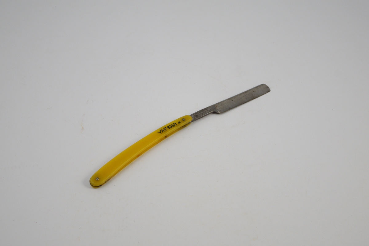 a) Rektangulær kniv, innhukk og smalere flate mot festet. Håndtak: to deler festet m/to skruer, ovale, noe buet form. Kniven kan vris inn mellom disse delene. 
b) Futeral, transparent på den ene side , buet, langstrakt form.