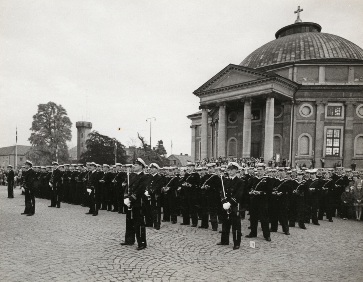 Marinens militärer poserar framför Tyska kyrkan. Matroserna bär eldvapen och sjöbefälen värjor.