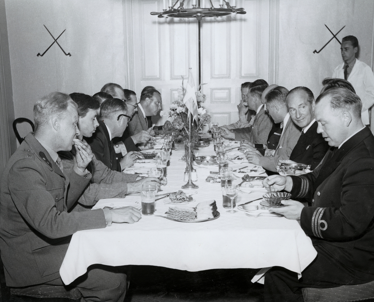 Militärklädda och civilklädda män sitter vid ett dukat middagsbord och intar en middag. Kommendörkapten Lind af Hageby på högra sidan med ansiktet vänt mot kameran.