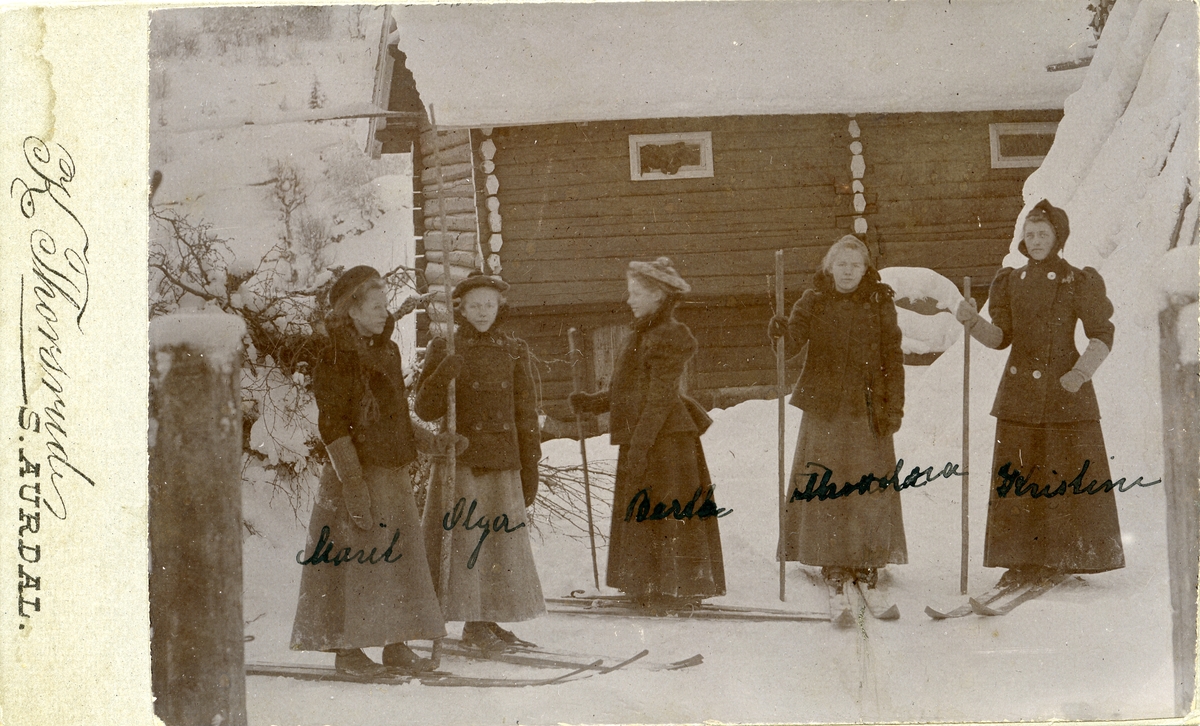 Fem unge kvinner står ute på gårdstunet med ski på beina.
