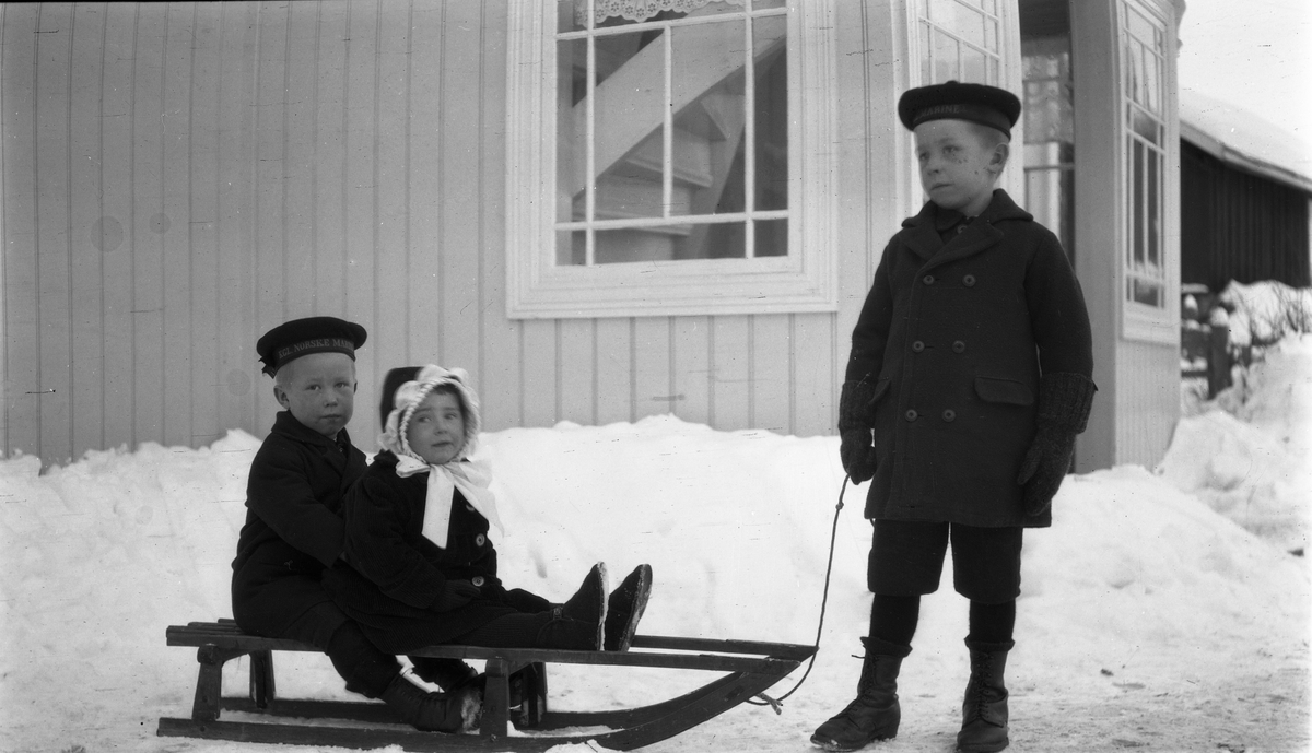 Tre barn og en kjelke. Barna er de tre eldste på gården Krabysanden, Østre Toten: Kåre (foran), Leif og Nora Gunnerød.