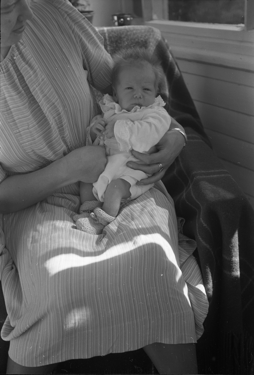 Uidentifisert lite barn. Serie på 10 Bilder. På noen av bildene holdes barnet av kvinner som bare delvis vises, og som heller ikke er identifisert.