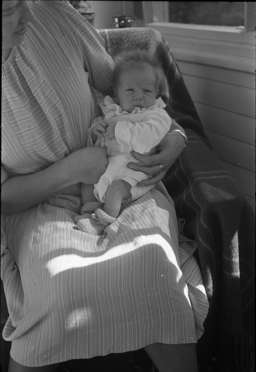 Uidentifisert lite barn. Serie på 10 Bilder. På noen av bildene holdes barnet av kvinner som bare delvis vises, og som heller ikke er identifisert.