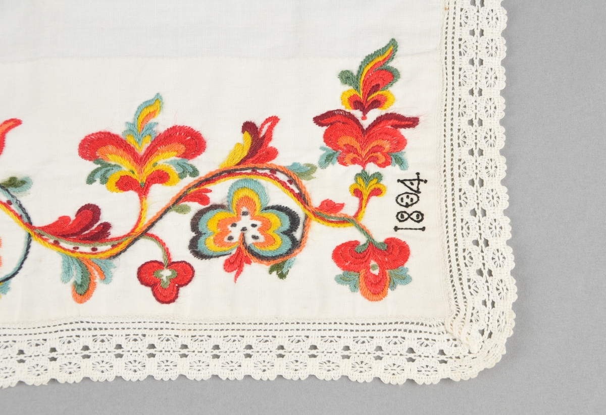 Kinnlag i kvitt linlerret, utsauma med ullgarn ("kamelgarn"), i raudt, grønt, gult, blått, orange og svart. Borden er sauma gjennom dobbelt tøy. Påsydd kvit bomullsblonde på tre sider, jarekant på kortsidene og falda på langsida.