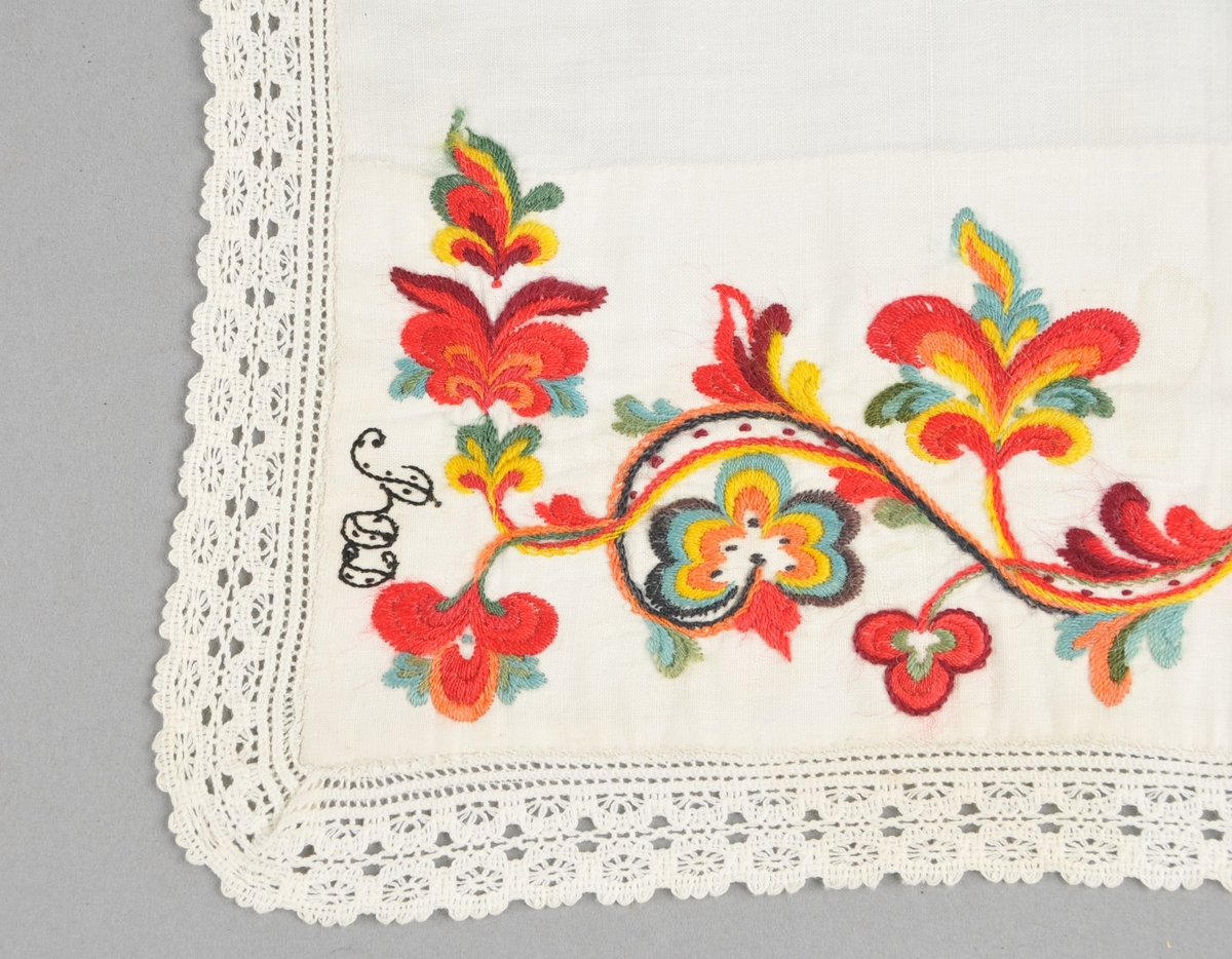 Kinnlag i kvitt linlerret, utsauma med ullgarn ("kamelgarn"), i raudt, grønt, gult, blått, orange og svart. Borden er sauma gjennom dobbelt tøy. Påsydd kvit bomullsblonde på tre sider, jarekant på kortsidene og falda på langsida.