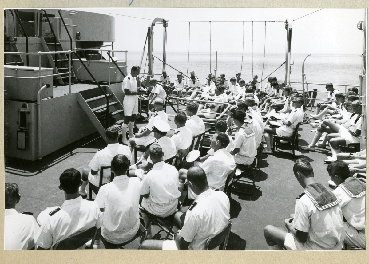 Bilden föreställer minfartyget Älvsnabbens besättning som sitter samlade i en gudstjänst på fartygets däck, klädda i vita sommaruniformer. Bilden är tagen under långresan 1966-1967.
