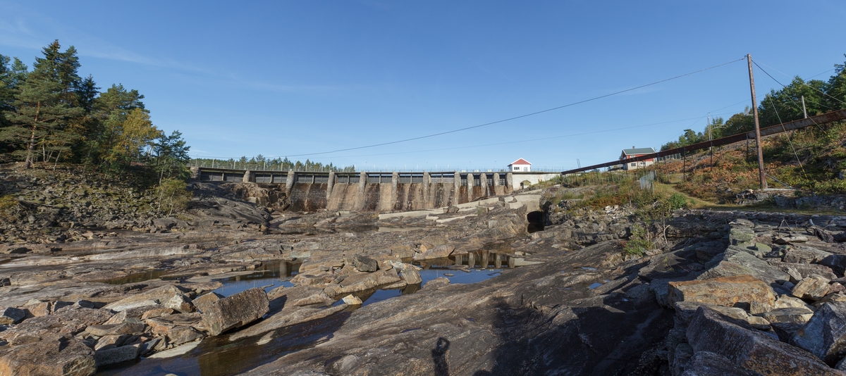 Haugsjå dam. Panoramafoto av Haugsjådammen nedstrøms. Dammen har 19 luker, på høgre side av dammen, under lukehuset (kvite vegger, rødt tak) ser vi bunnløpet. På høgre side av dammen går tømmerrenna ned forbi Bøylefoss kraftstasjon. Sett mot NV.