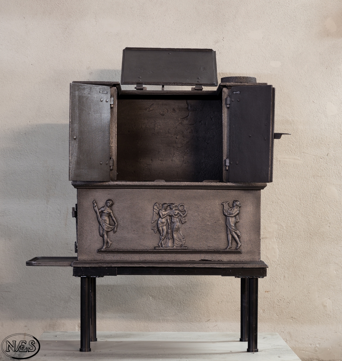 Kokeovn i to etasjer med eget fyrkammer og kokerom. Kokerommet kan åpnes med to dører på langsiden og med en luke i topplaten. Ovnsdøren til fyrkammeret er på kortsiden 1 etg. På langsidene i 1. etg er det tre muser og en engel med lette draperier på en enkel profillist. På kortsidene 2. etg er det draperikledd dansende muse på enkel profillist med en rosett i hvert øvre hjørne. Langsidene i 2.etg er dekorert med en rosett i hvert øvre hjørne.