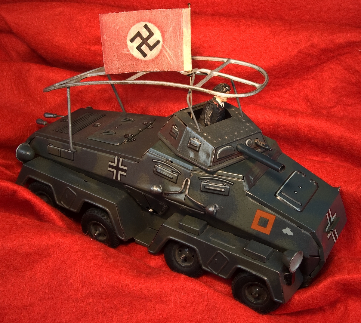 Leksaksstridsvagn av lithograferad plåt. Mörkt grön med dekorationer i rött och vit/svart. Okänd tillverkning. Saknar stämplar. Till stridsvagnen finns en soldat, förmodligen av elastolin, en nazistflagga samt en nyckel för uppskruvning.