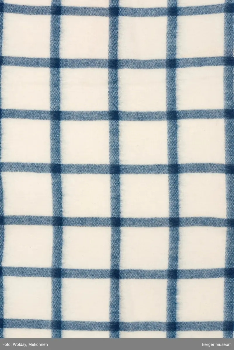 En pleddprøve i rutemønster. Prøven har klippede langsider, jarekant på kortsidene.  Mønsteret karakterisereres av blå striper i kvadratisk rutemønster på hvit bunn.