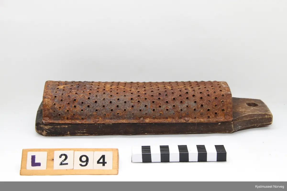 Potetrasp. Laget ved at et trestykke er tilskåret med opphengshull i ene enden, og stort hull inni som er tilpasset selve rivjernet. Rivjernet er utformet av et buet blikkstykke, der det er laget mange hull med spiker. Blikkstykket/rivjernet er spikret fast på trestykket.