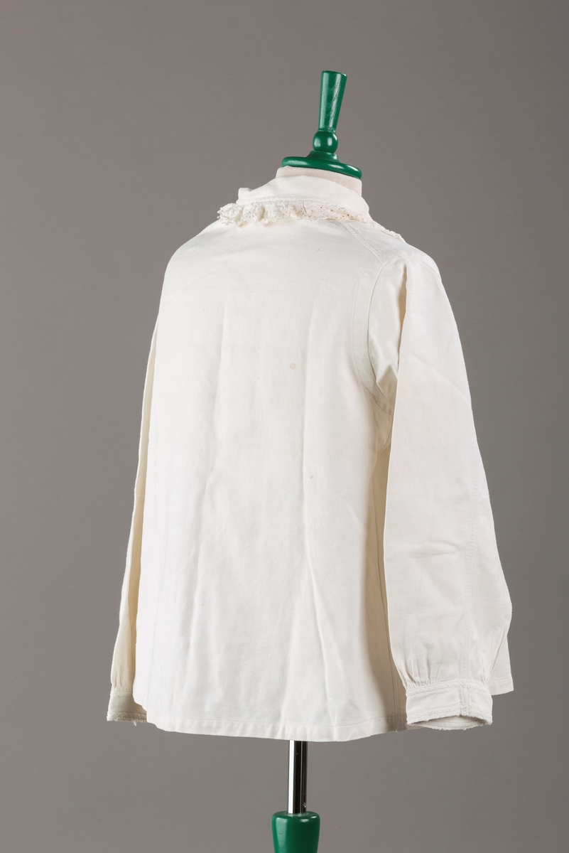 Form: Hoftelang trøye, Lange ermer, krage. Kragen og åpningen foran er kantet med  maskinprodusert blonde. Tre biser på hver side av åpn. foran. Lukkes med to løse knapper.