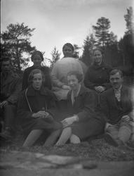 Gruppe på 7 voksne som sitter på bakken. Fra v. bak ukjent, 